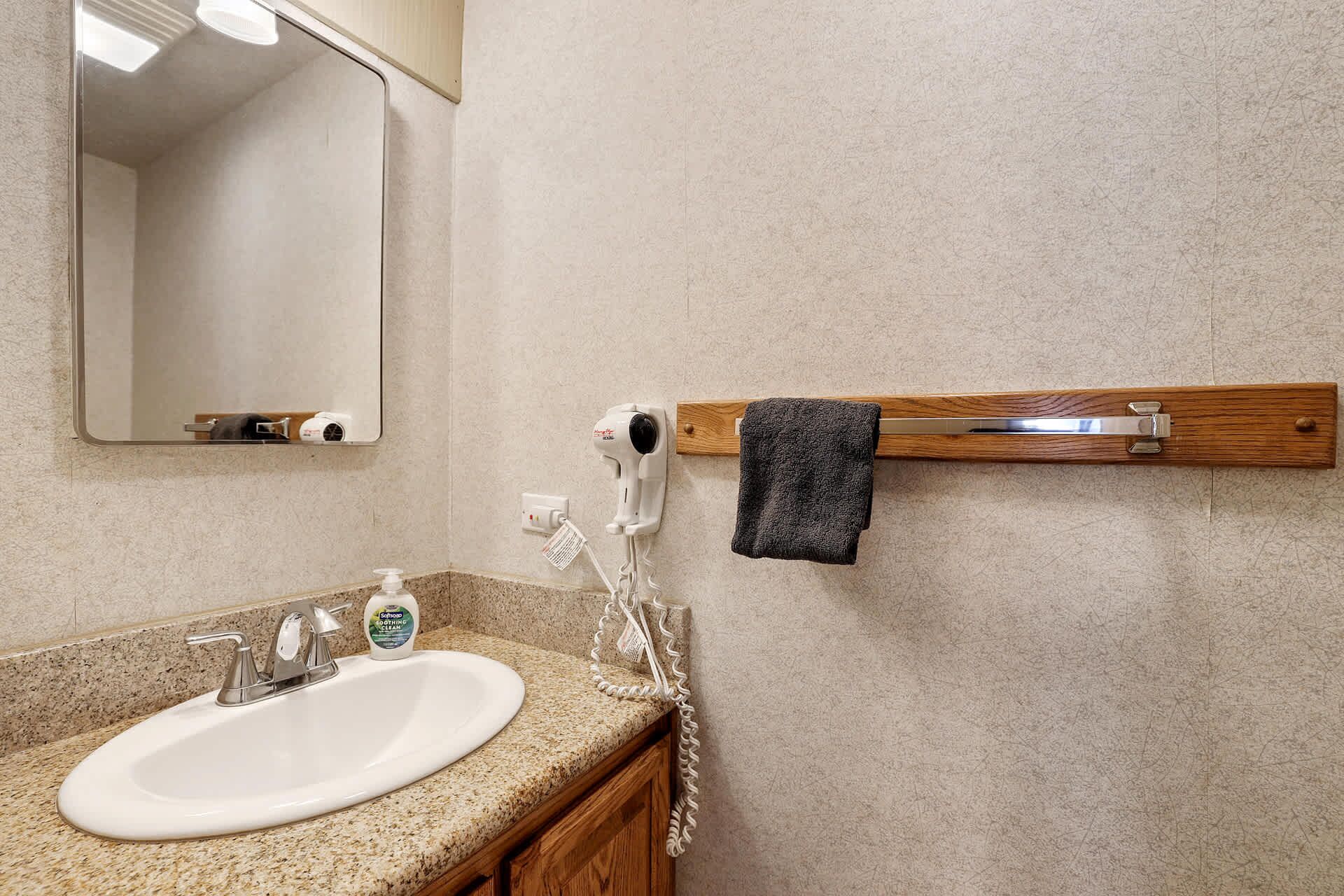 A bathroom with a granite countertop, a white sink, a mirror, a towel rack, and a hairdryer.