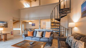 A spacious living area with a grey sofa, a wooden coffee table, and a staircase leading to an upper level.