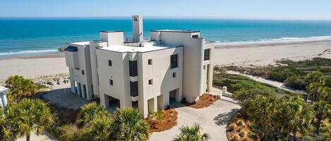 A modern, multi-story building with a flat roof, situated on a beachfront with a clear view of the ocean.