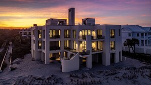 Un hôtel moderne à plusieurs étages, doté de balcons et de grandes fenêtres, situé sur une plage offrant une vue imprenable sur le coucher de soleil.