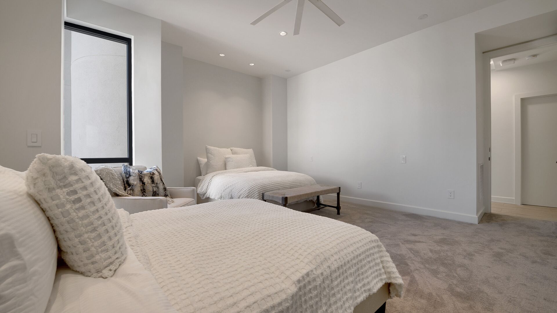 A spacious bedroom with two beds, a large window, and a door leading to another room.