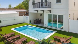 Ein zweistöckiges Haus mit Swimmingpool, Balkon und einer Terrasse mit Gartenmöbeln.