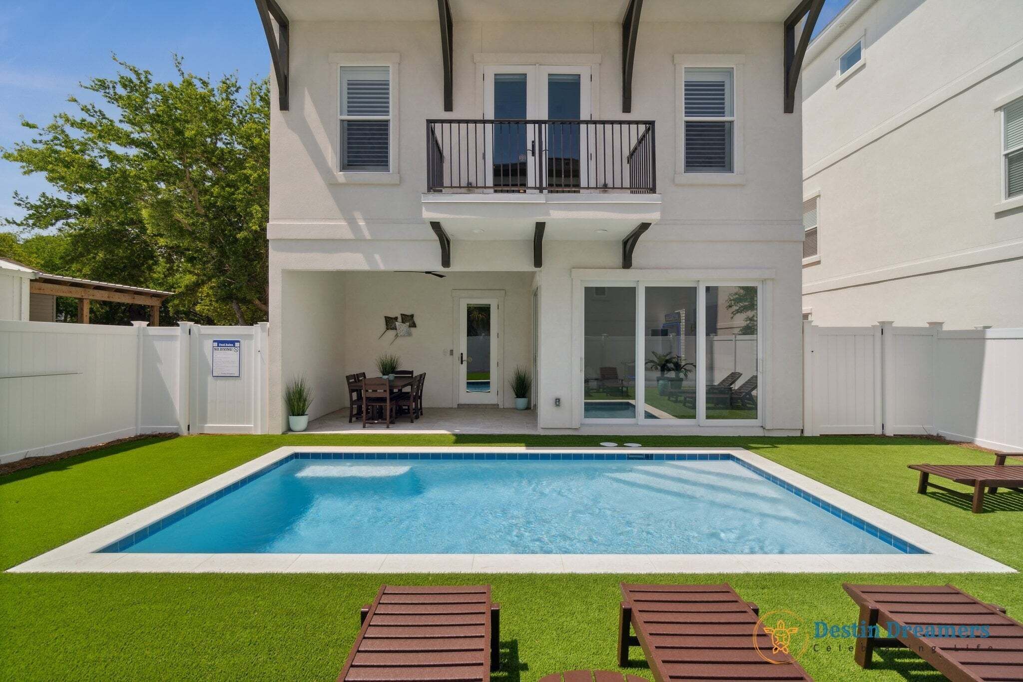 Una casa de dos pisos con piscina, balcón y zona de patio con sillas de descanso.