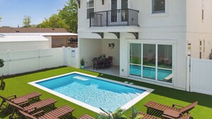 A two-story house with a swimming pool, a balcony, and a patio area with outdoor furniture.