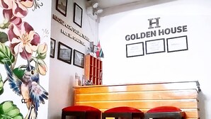 A restaurant interior with a wooden counter, red stools, and a wall with floral artwork and a sign reading "Golden House". - Golden House Hotel  (Cusco)