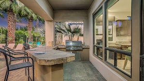 An outdoor kitchen area with a grill, seating, and a view of the interior.
