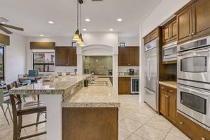 A modern kitchen with granite countertops, stainless steel appliances, and wooden cabinetry. - Casa De Amore: Pool, Spa, Casitas, Built-n BBQ! (Indio)