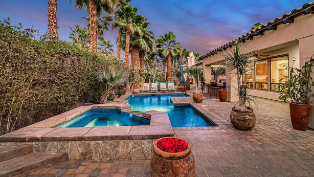 A pool area with two pools, surrounded by palm trees and potted plants.