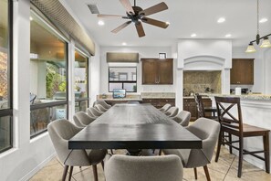 A spacious dining area with a long table and multiple chairs, a ceiling fan, and a kitchen area with granite countertops. - Casa De Amore: Pool, Spa, Casitas, Built-n BBQ! (Indio)