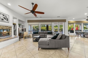 A spacious living room with a fireplace, a large sofa, and a ceiling fan. - Casa De Amore: Pool, Spa, Casitas, Built-n BBQ! (Indio)