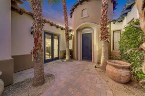 A courtyard with a paved walkway, palm trees, and a building with a blue door. - Casa De Amore: Pool, Spa, Casitas, Built-n BBQ! (Indio)