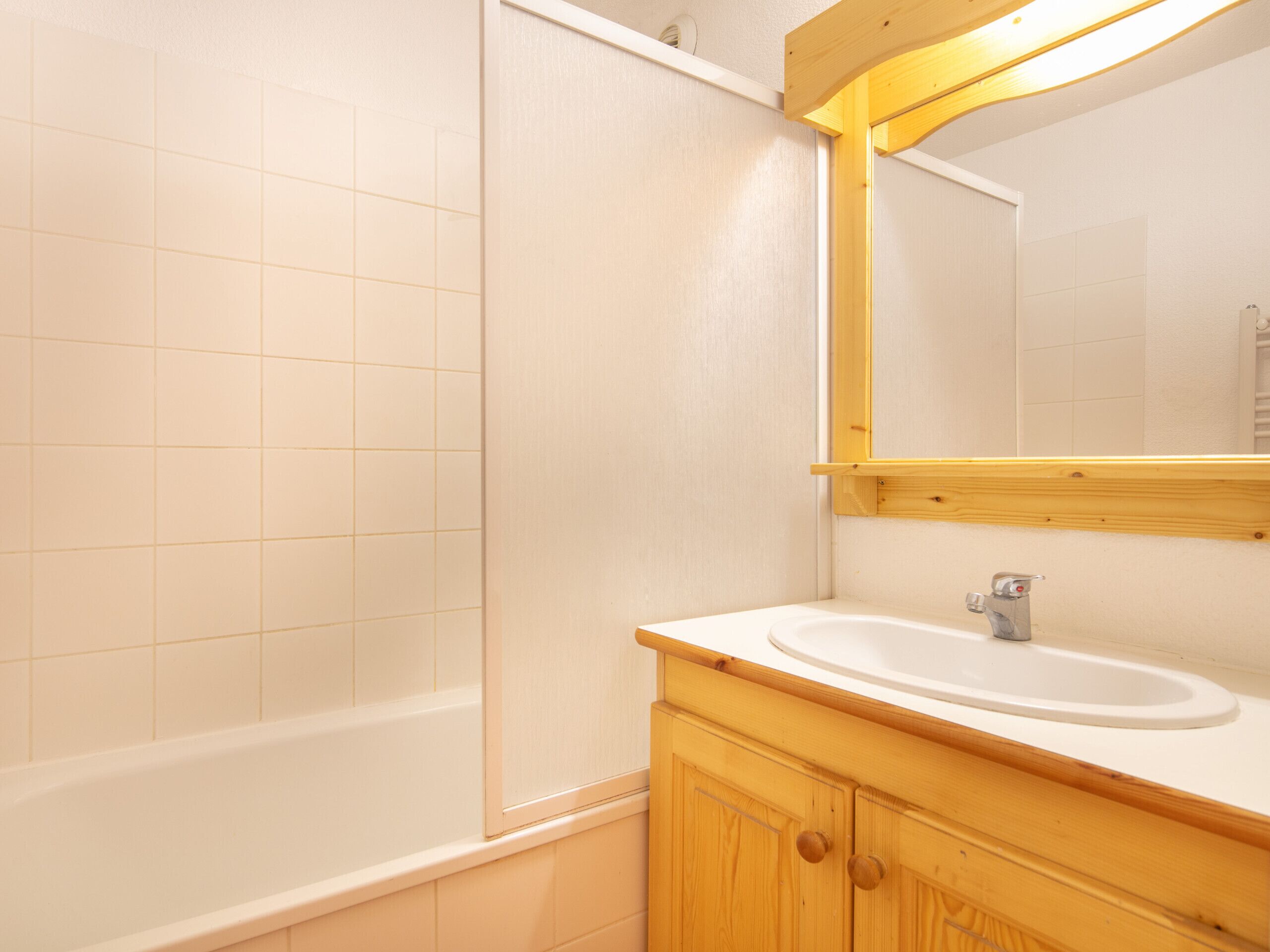 Een badkamer met een bad, een wastafel, houten kastjes en een spiegel.