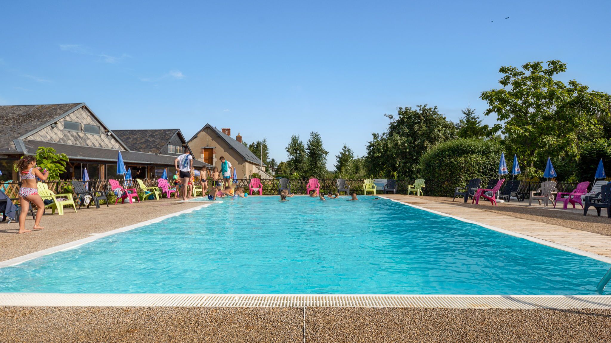 Una piscina con persone che nuotano e si rilassano. Sono presenti sedie a sdraio colorate e ombrelloni.