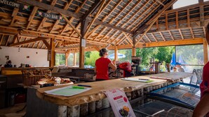 Una zona de bar con barra de madera, un letrero que dice 'Welcome', un letrero que dice 'Tiki Bar' y una pizarra con el menú.