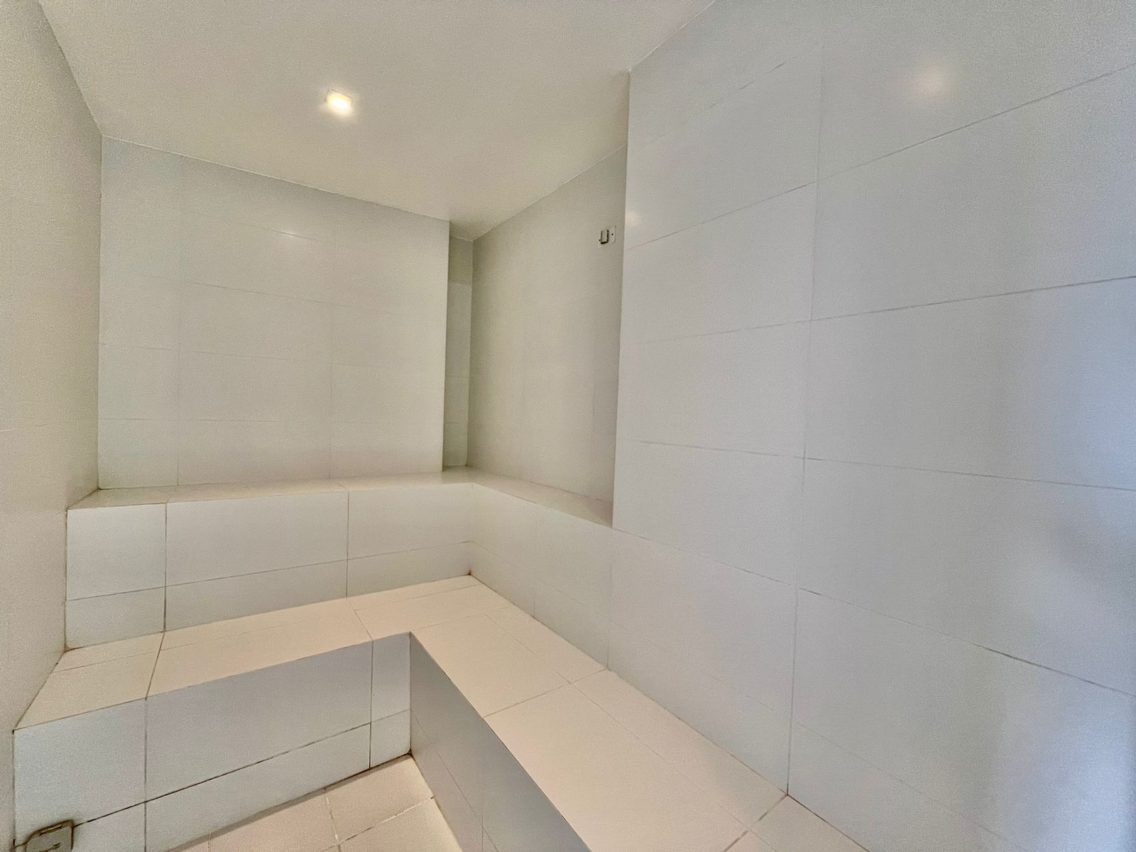 A modern bathroom with white tiles, a built-in bench, and a recessed ceiling light.