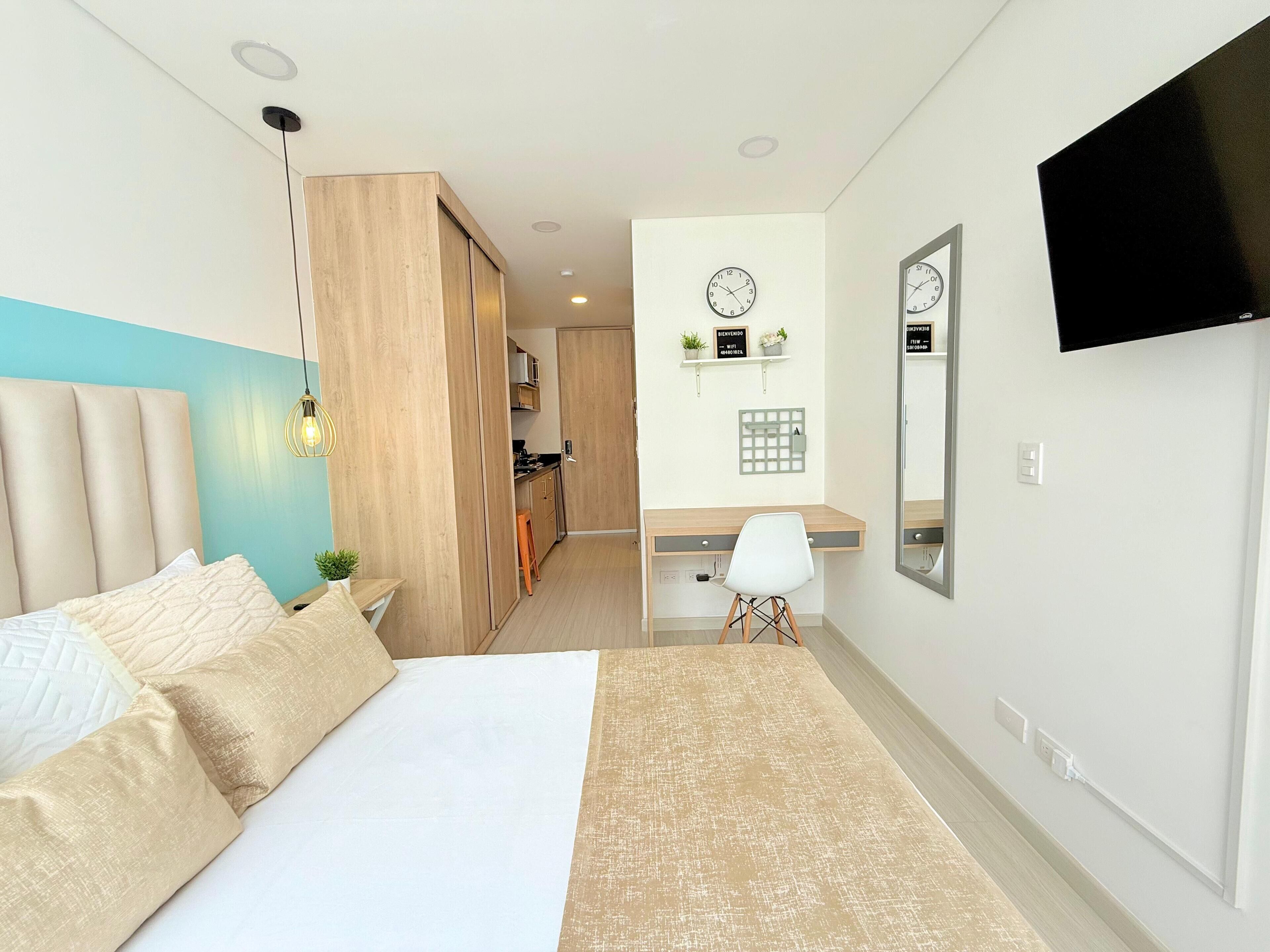 Une chambre d’hôtel avec un lit, un bureau, une chaise, une télévision, une horloge et une petite plante accrochée au mur.