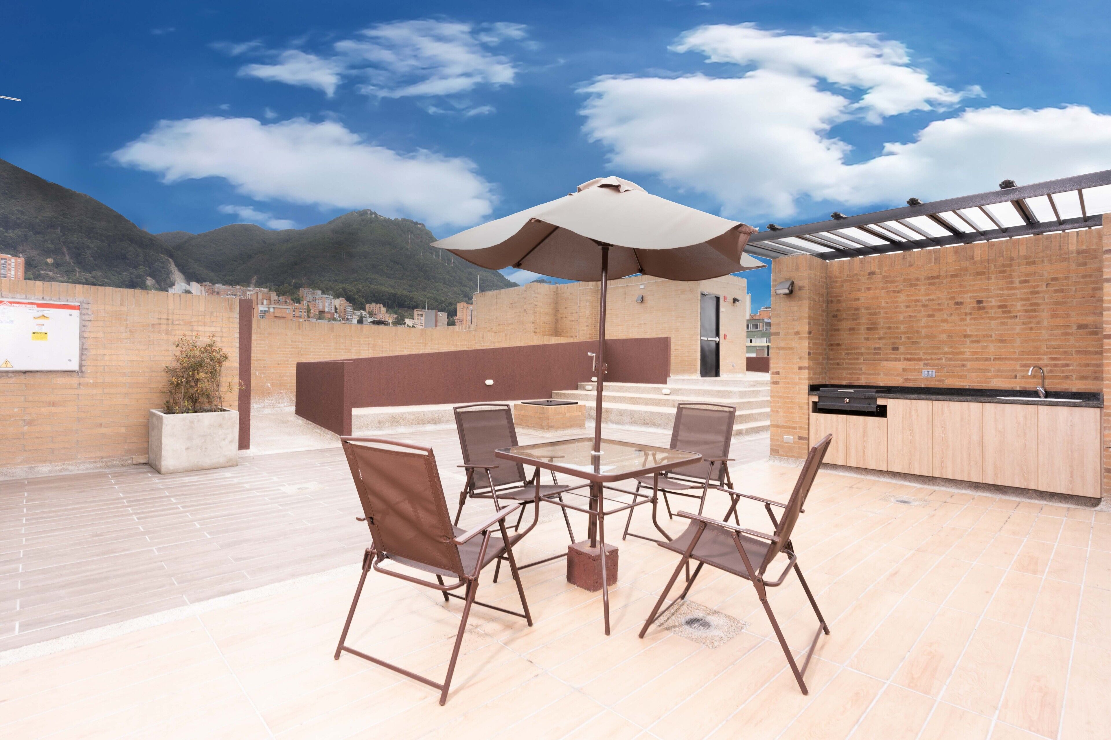 Un patio al aire libre con una mesa, sillas, un paraguas grande y una zona de cocina.