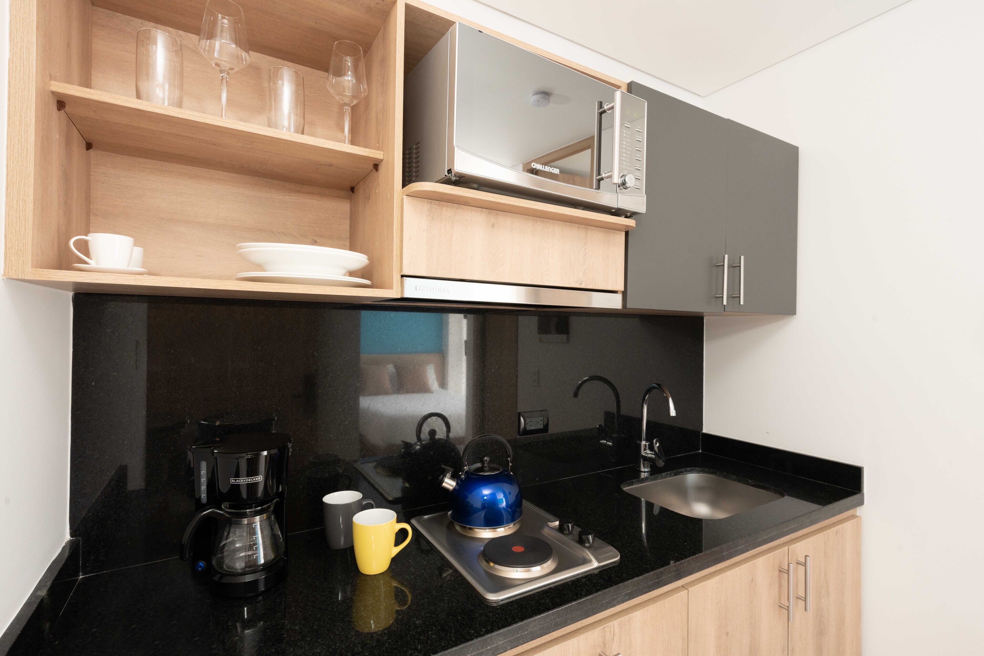 A modern kitchen with a coffee maker, kettle, and microwave on the counter, and wooden shelves above.