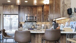 A kitchen with wooden cabinets, stainless steel appliances, and bar stools. - Kirkwood Mountainside Cabin w/Views, Walk to Lifts (Kirkwood)