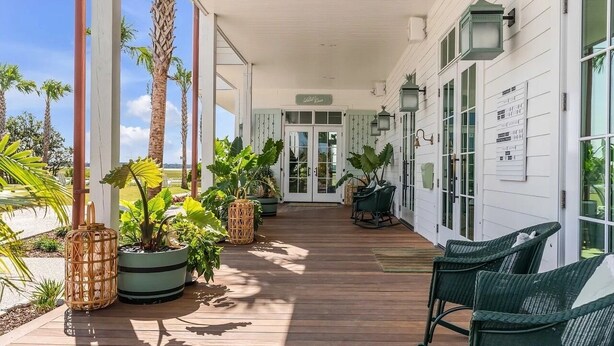 Une véranda couverte avec un plancher en bois, des plantes en pot, des fauteuils en osier et une pancarte sur laquelle on peut lire « Bienvenue ».
