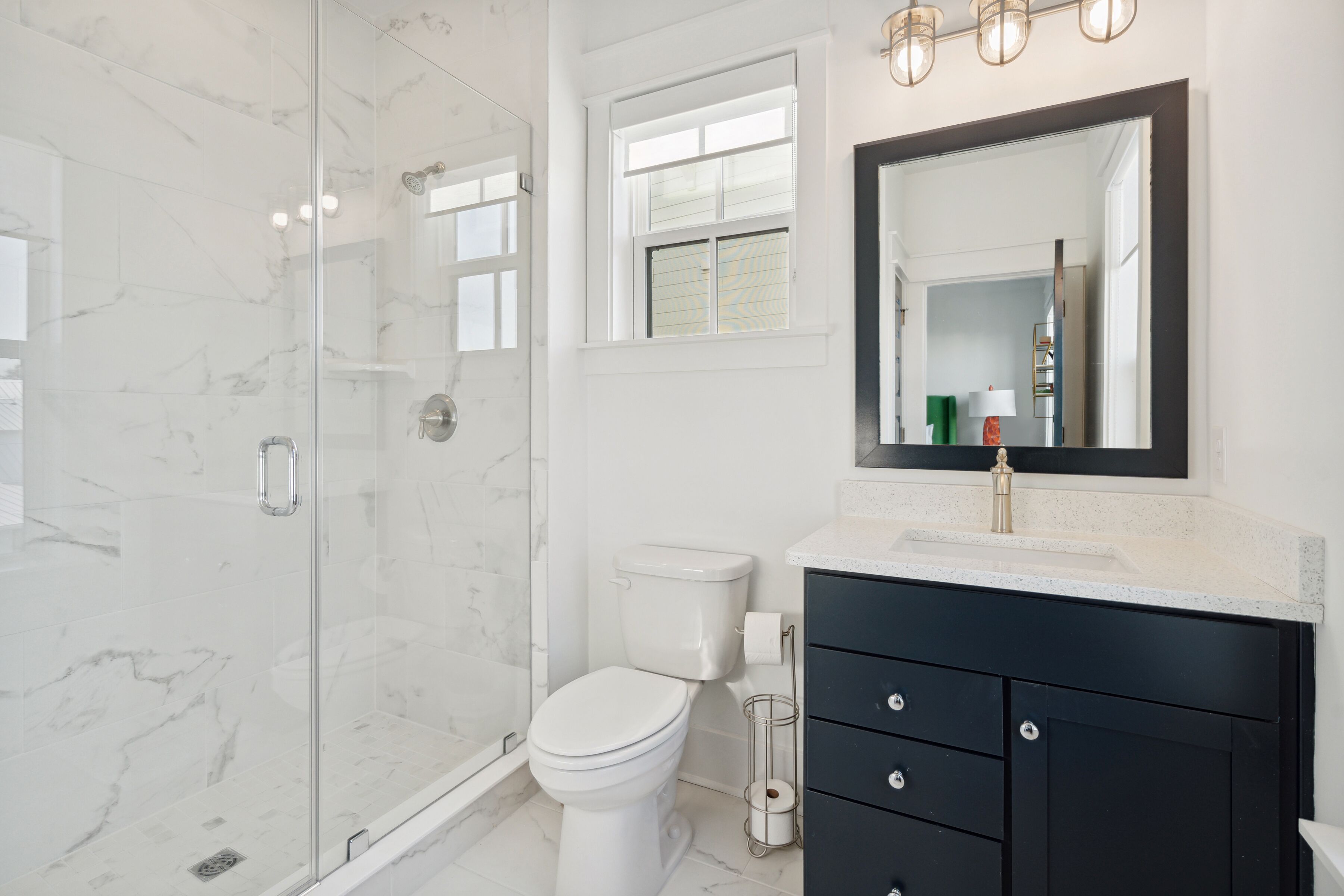 A modern bathroom with a glass-enclosed shower, a white toilet, and a dark vanity with a mirror above.
