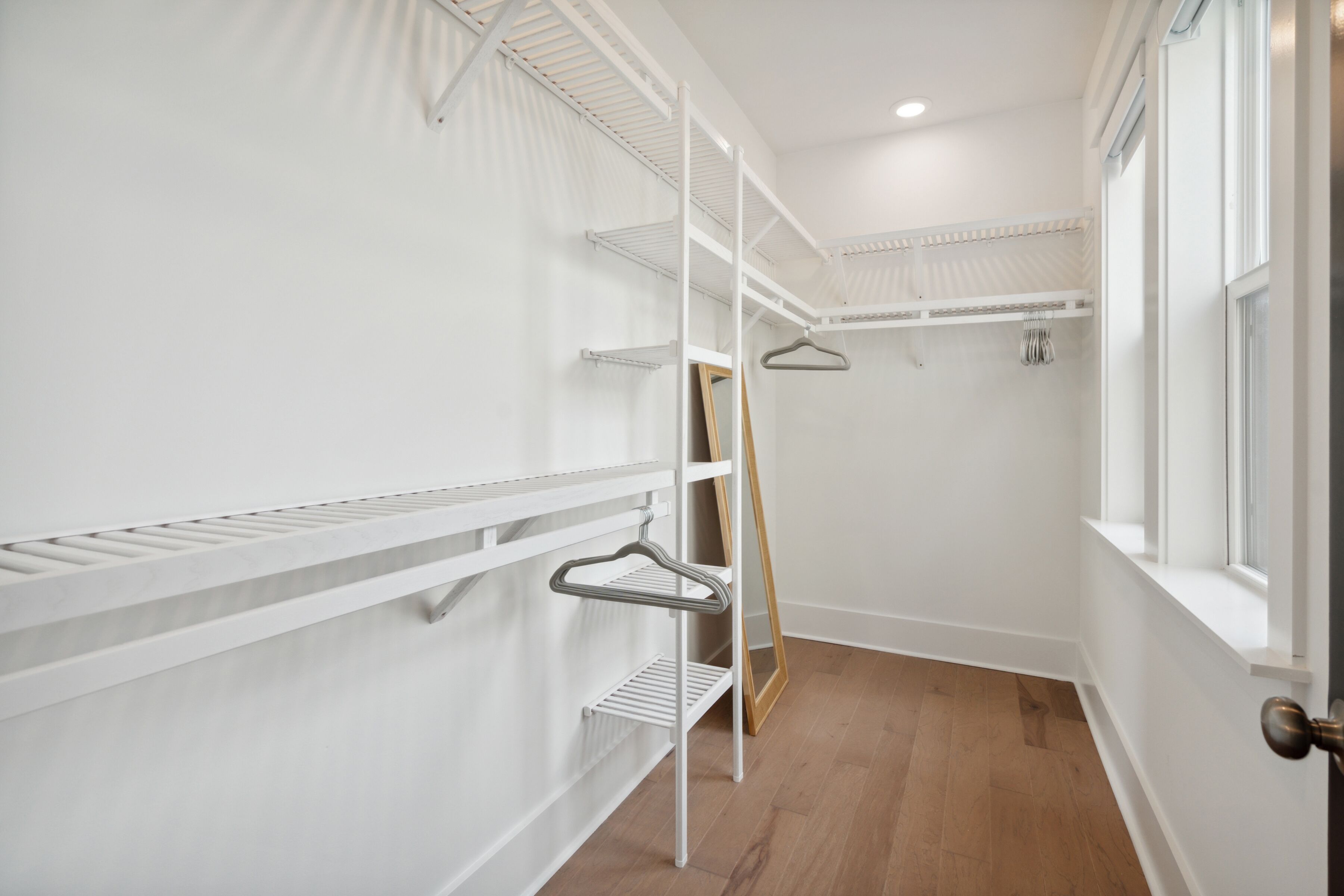 Un dressing avec des étagères blanches, un miroir et une tringle pour suspendre les vêtements.