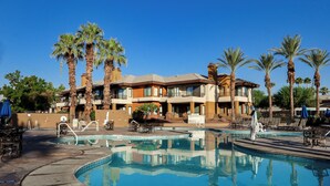 A hotel with a swimming pool, palm trees, and lounge chairs.