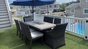 A patio with a table and chairs, a blue umbrella, and a view of neighboring houses. - Short Block to The Beach! Newly Remodeled With Pool & Hot Tub! (Brant Beach)