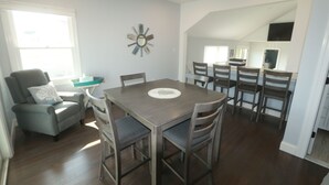A dining area with a wooden table and chairs, a gray armchair, and a decorative mirror on the wall. - Short Block to The Beach! Newly Remodeled With Pool & Hot Tub! (Brant Beach)