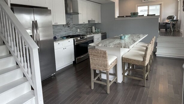 A modern kitchen with white cabinets, a stainless steel refrigerator, a marble island, and a staircase leading to another level. - Short Block to The Beach! Newly Remodeled With Pool & Hot Tub! (Brant Beach)