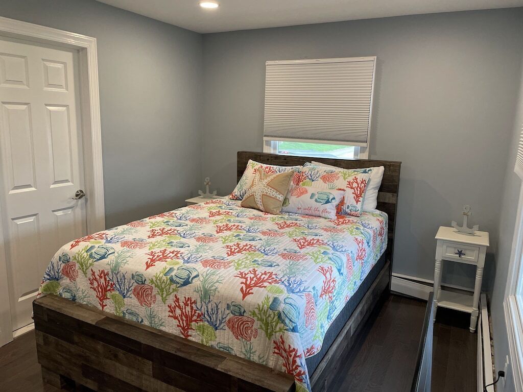 Un dormitorio con una cama, una mesita de noche, una ventana con persianas y una puerta.
