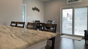 A dining area with a marble table, wooden chairs, and a view of the city through a glass door. - Short Block to The Beach! Newly Remodeled With Pool & Hot Tub! (Brant Beach)