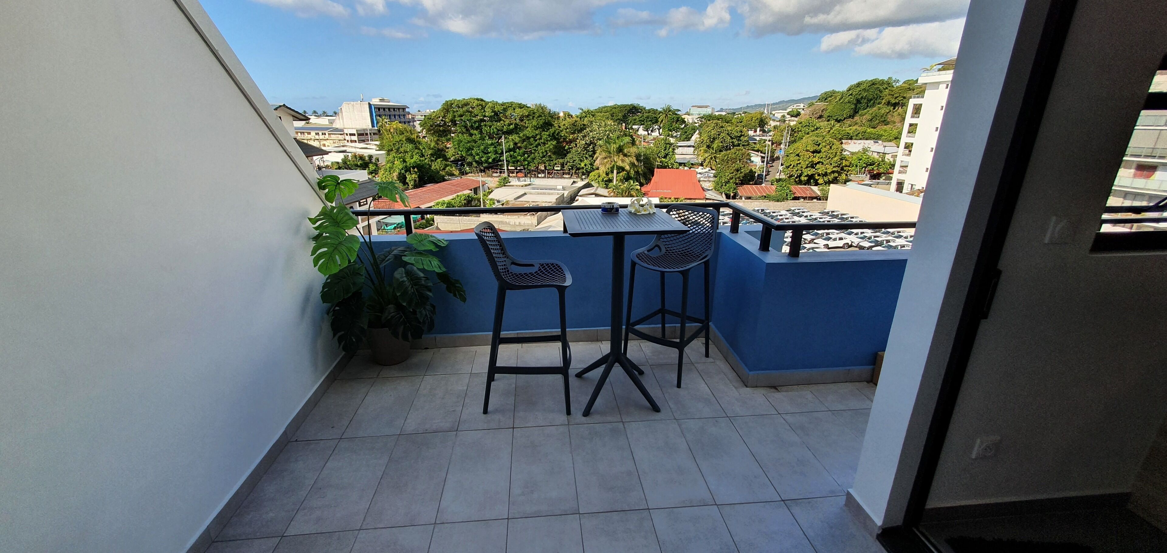 A balcony with two chairs and a table, a potted plant, and a view of buildings and trees.
