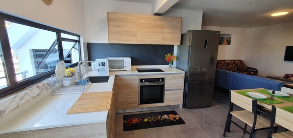 A modern kitchen with a built-in oven, microwave, and refrigerator. There is a dining area with a table and chairs, and a window providing a view of the outside.