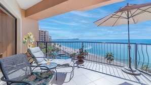 Ein Balkon mit Blick auf den Strand, ein Tisch mit Blumenvase und ein Stuhl.