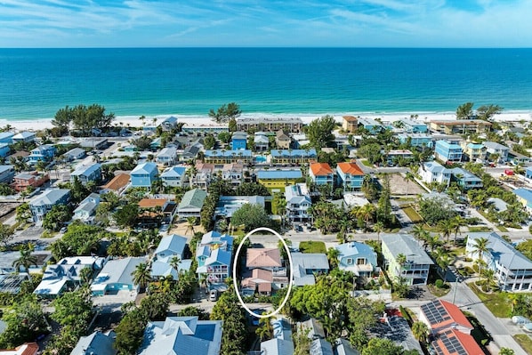 Vue aérienne d’une zone résidentielle côtière, avec des maisons, une plage et un ciel bleu dégagé.