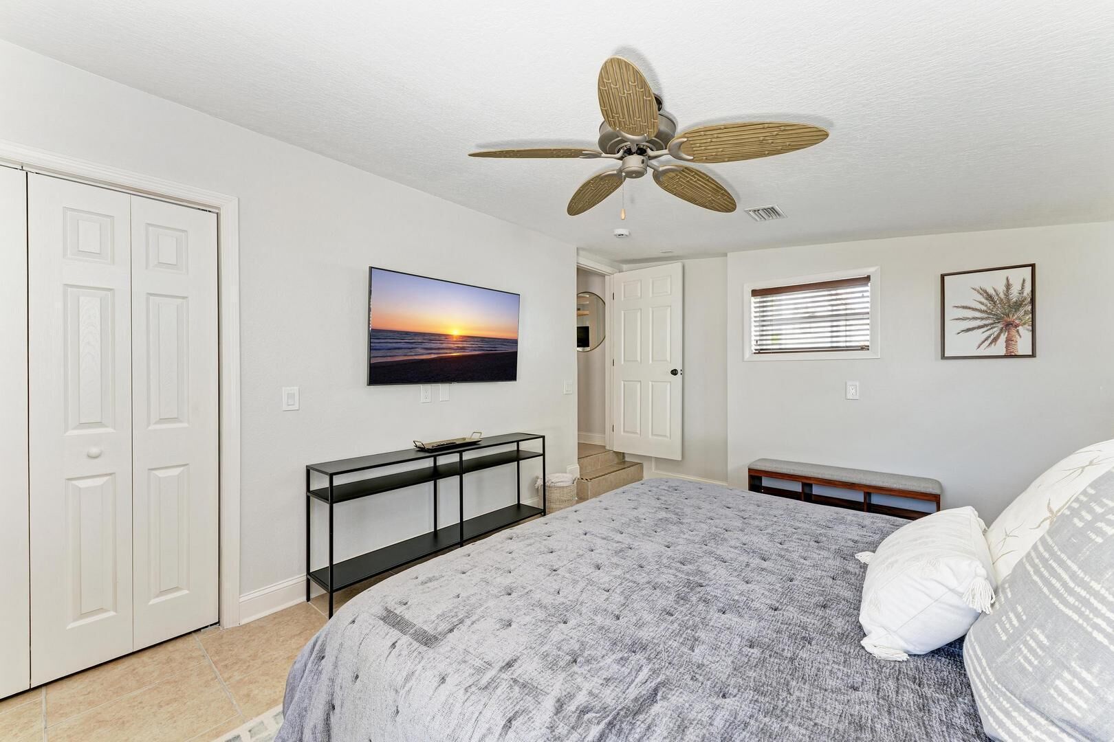 A bedroom with a bed, a ceiling fan, a TV, a console table, and a door.