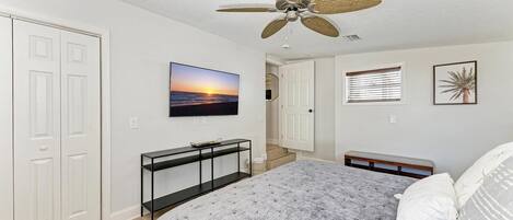 A bedroom with a bed, a ceiling fan, a TV, a console table, and a door.