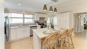 Una cocina moderna con armarios blancos, una isla central con taburetes y luminarias colgantes.