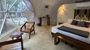 Habitación tipo tienda de campaña con cama, muebles de madera y vistas amplias a través de grandes ventanales.