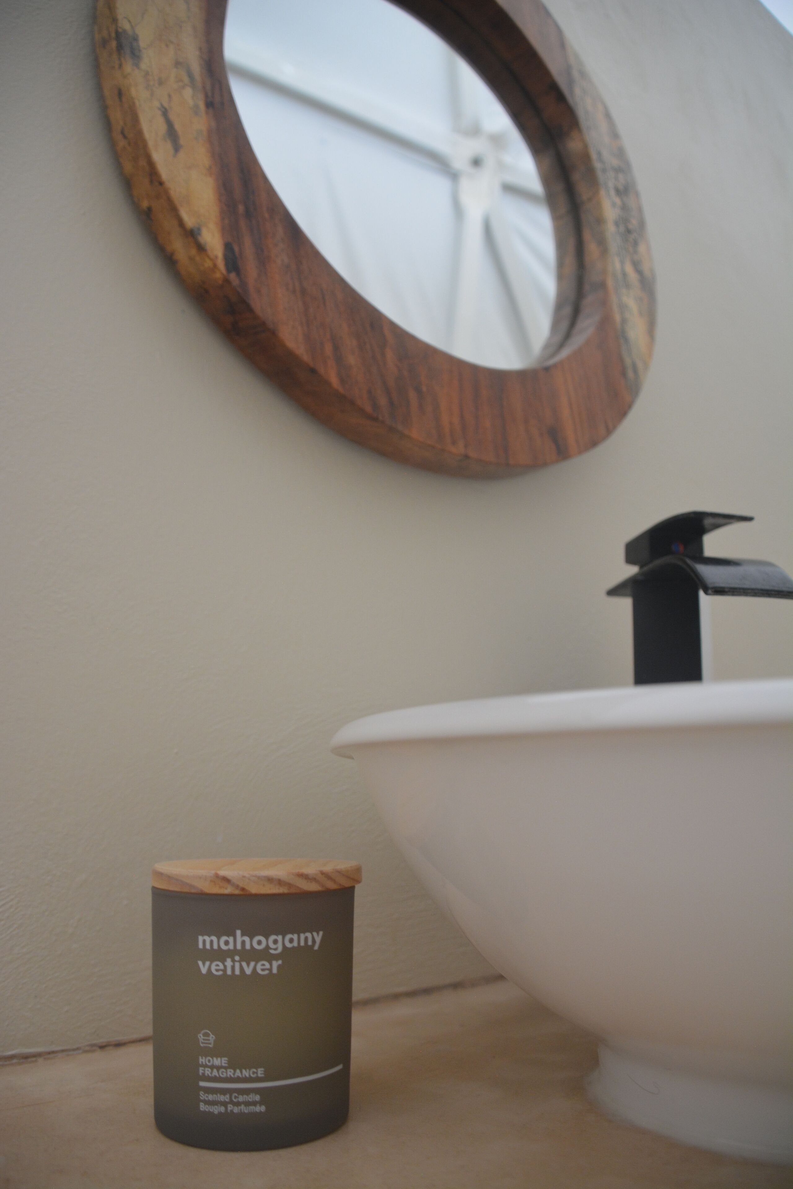 Ein Badezimmer mit einem spiegelnden Holzelement, einem weißen Waschbecken und einem Mahagoni-Duftkerzen mit Vetiver.