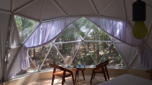 Una tienda en forma de cúpula con un ventanal grande, sillas de madera y una mesita.