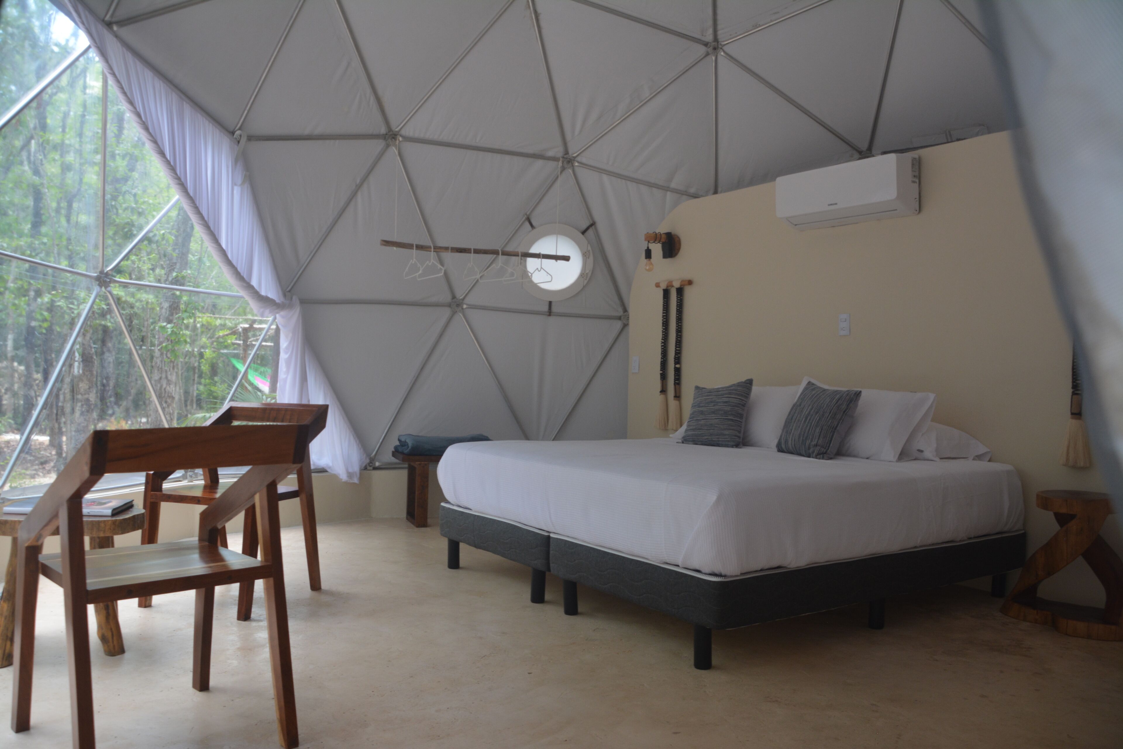 A tented accommodation with a bed, wooden furniture, and a view of trees.