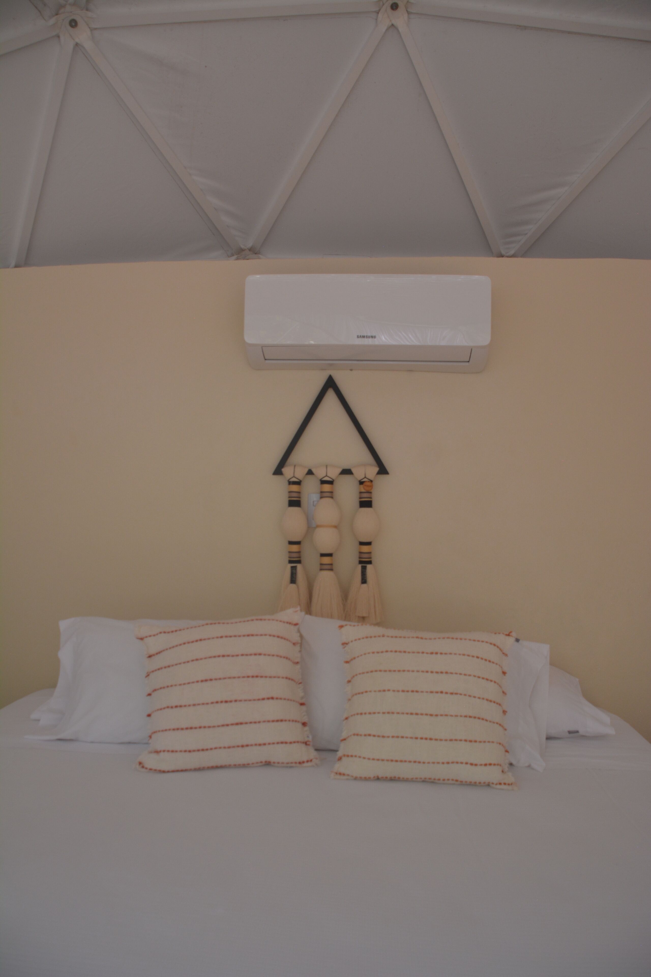 A bed with two pillows, a wall-mounted air conditioner, and a hanging light fixture.