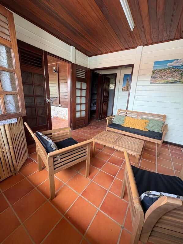 A room with a wooden ceiling, a sofa with cushions, a small table, and a tiled floor. - 2 air-conditioned bedrooms, 5 mins walk from the beach, wifi , jacuzzi , garden (Le Vauclin)