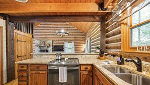 A log cabin kitchen with a central island, granite countertops, and a stainless steel stove. - Hocking Hills Secluded Cabin • Hot Tub • Fireplace (Logan)