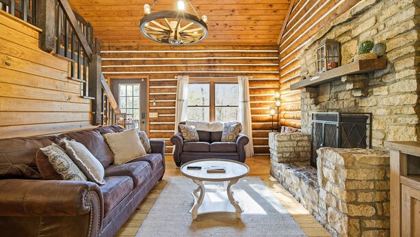A log cabin interior with a leather sofa, two armchairs, a coffee table, and a stone fireplace. - Hocking Hills Secluded Cabin • Hot Tub • Fireplace (Logan)