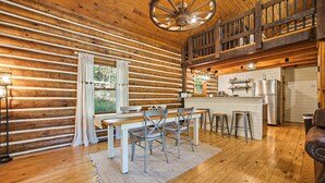A log cabin interior with a dining area, kitchen, and a balcony. - Hocking Hills Secluded Cabin • Hot Tub • Fireplace (Logan)
