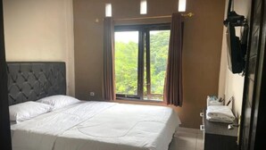 Un dormitori amb un llit, una finestra amb cortines, una taula de nit amb una làmpada i un televisor fixat a la paret.