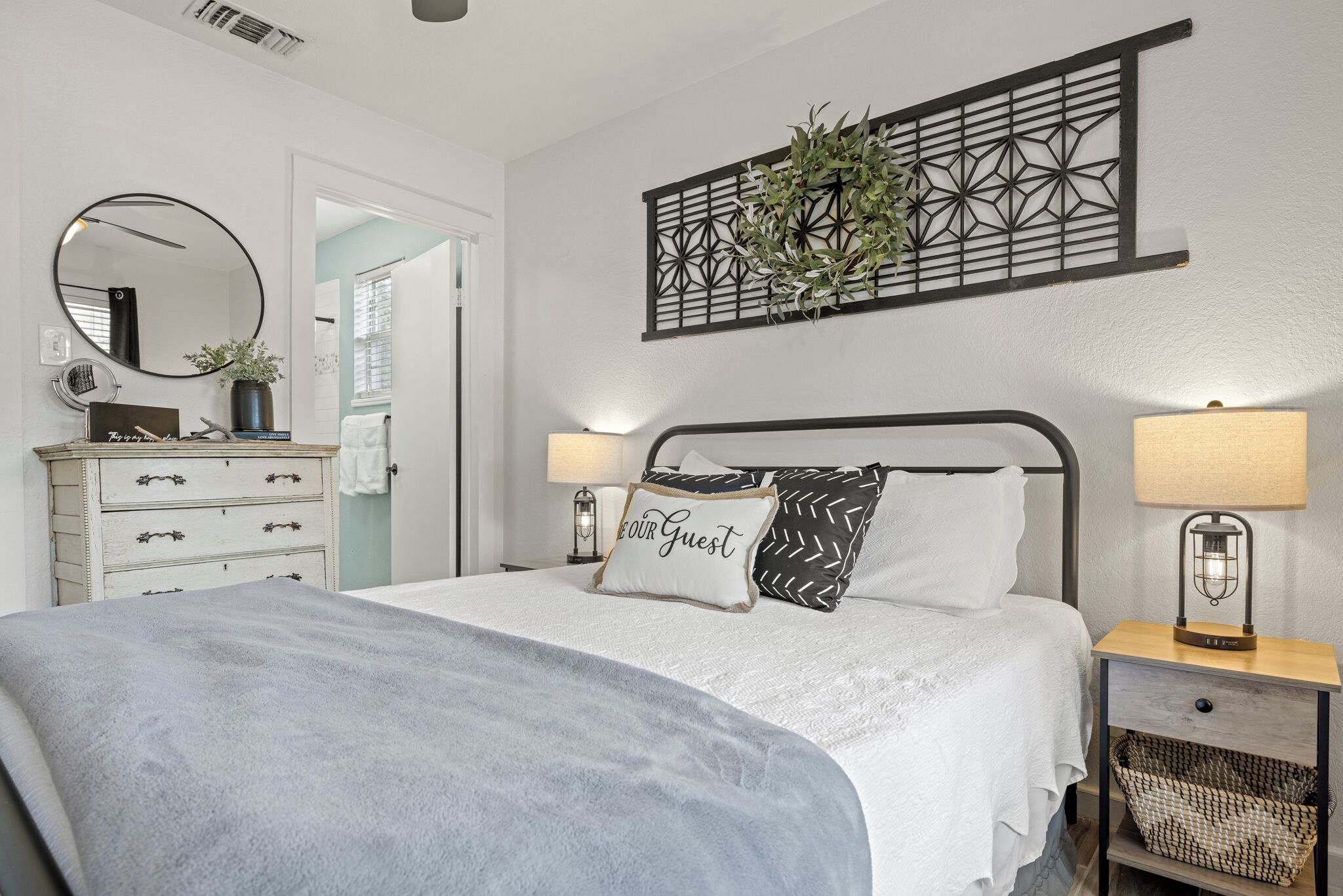 Une chambre à coucher bien rangée, avec un lit, des tables de chevet, une commode, un miroir et un élément décoratif mural.